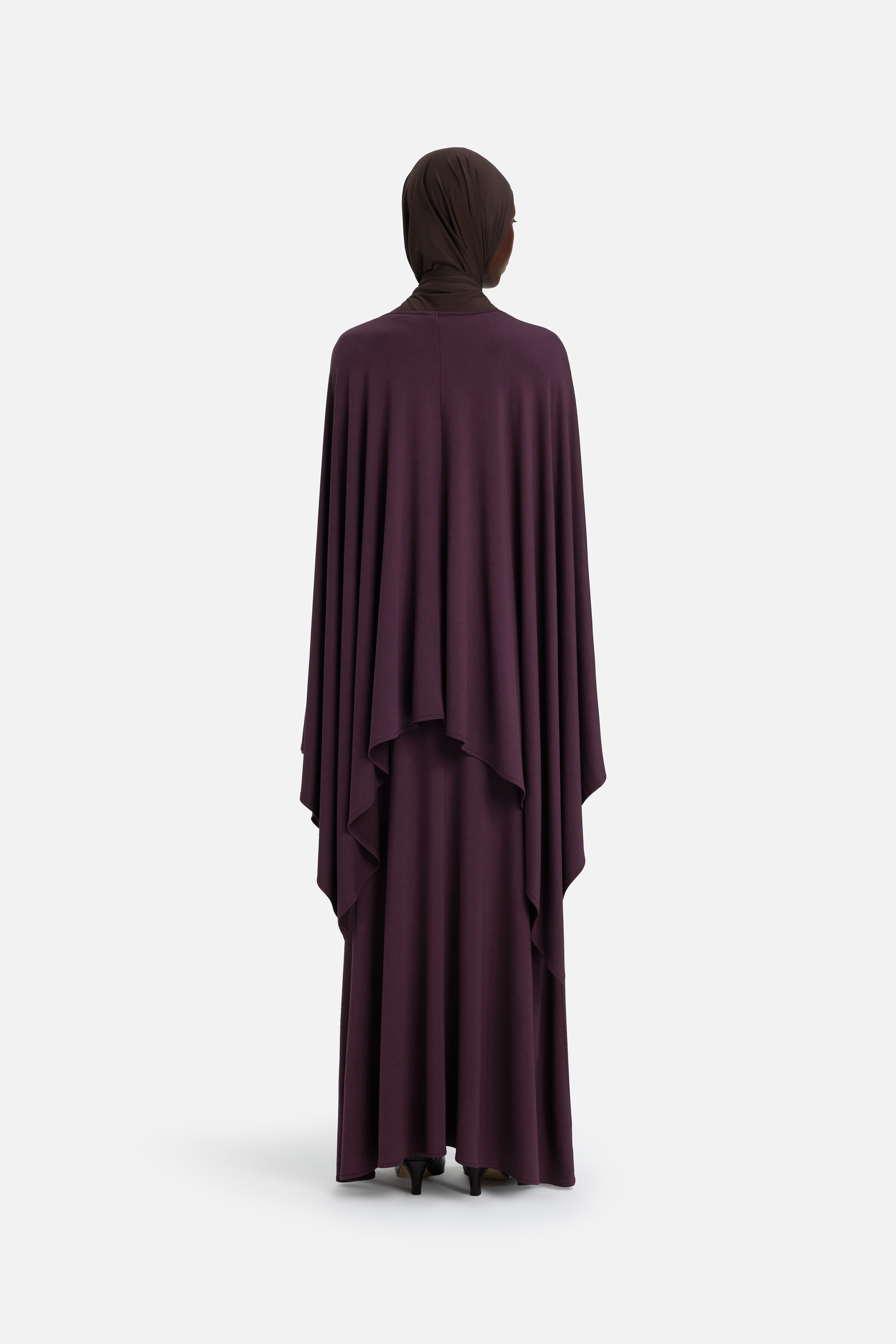Model wearing purple cape and brown headscarf, back view