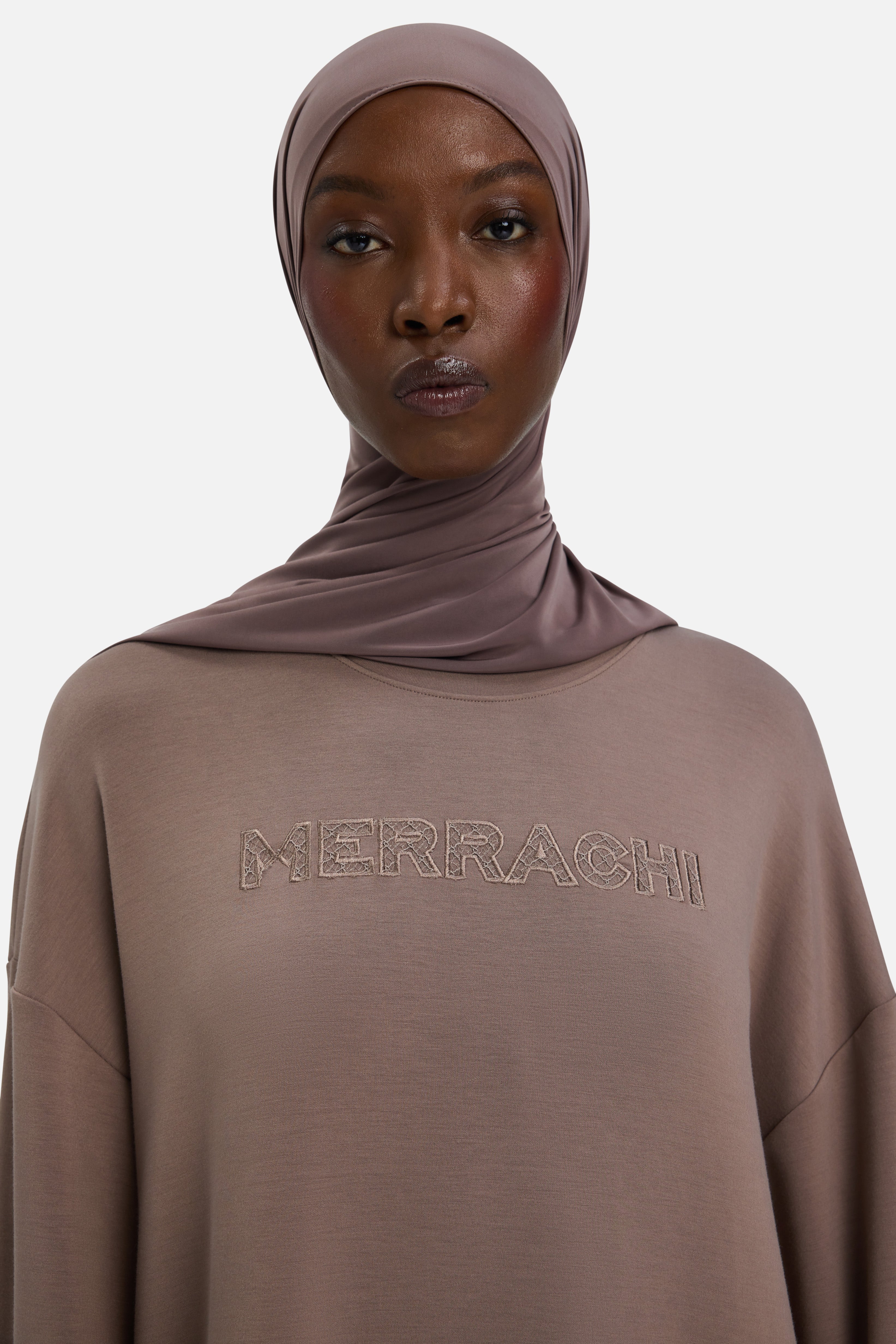 Model wearing purple headscarf and dress with MERRACHI embroidery