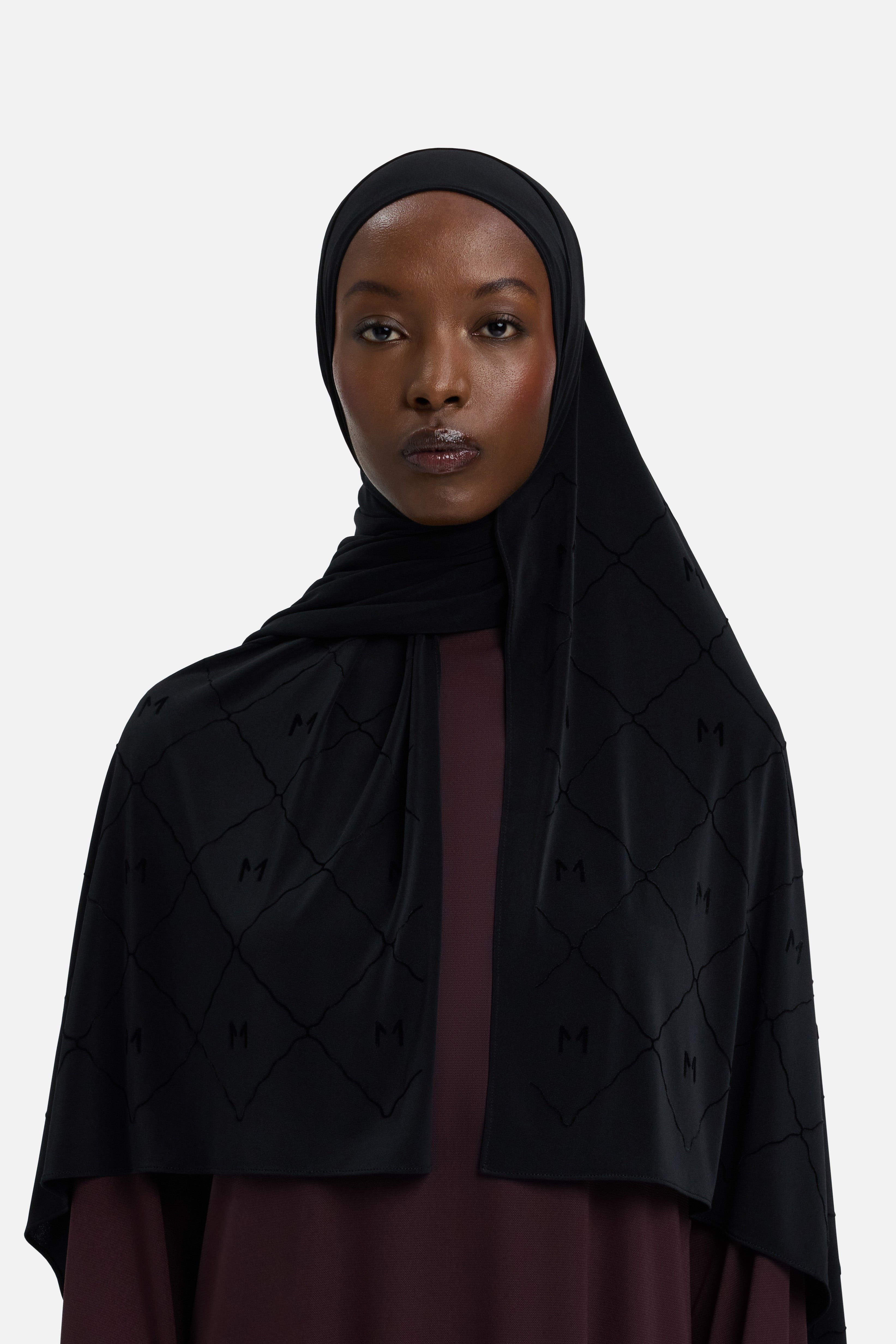 Model wearing black headscarf MERRACHI logo and embroidery, front view