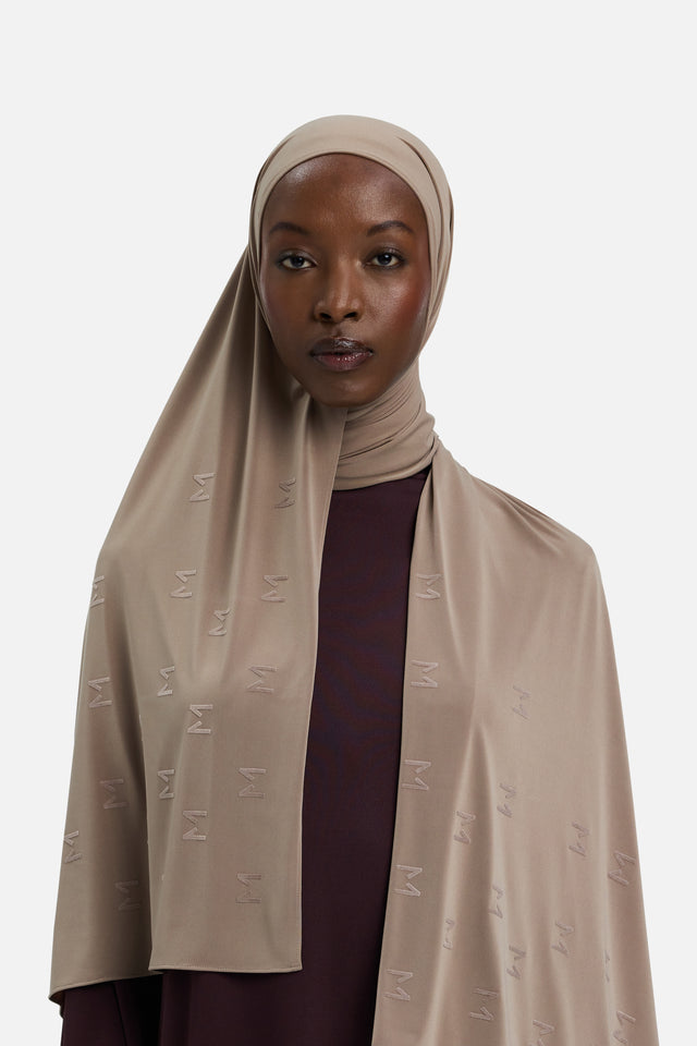 Model wearing taupe headscarf MERRACHI logo embroidery, front view